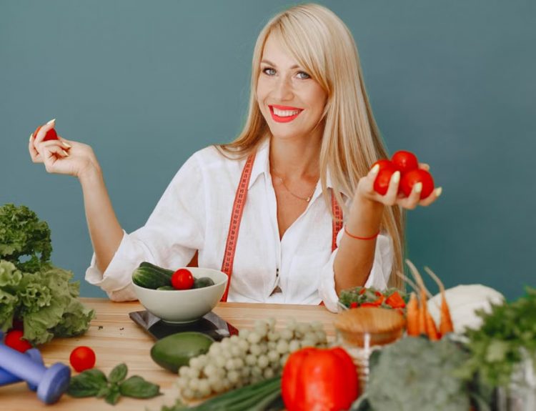 Healthy lifestyle concept with woman holding tomatoes and surrounded by fresh vegetables in a studio setting.