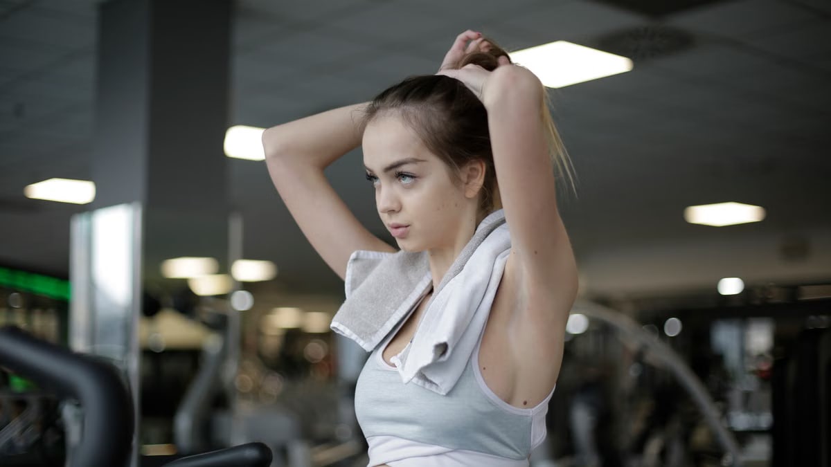 Woman adjusting ponytail in gym, ready to start her fitness routine. Determined and focused.