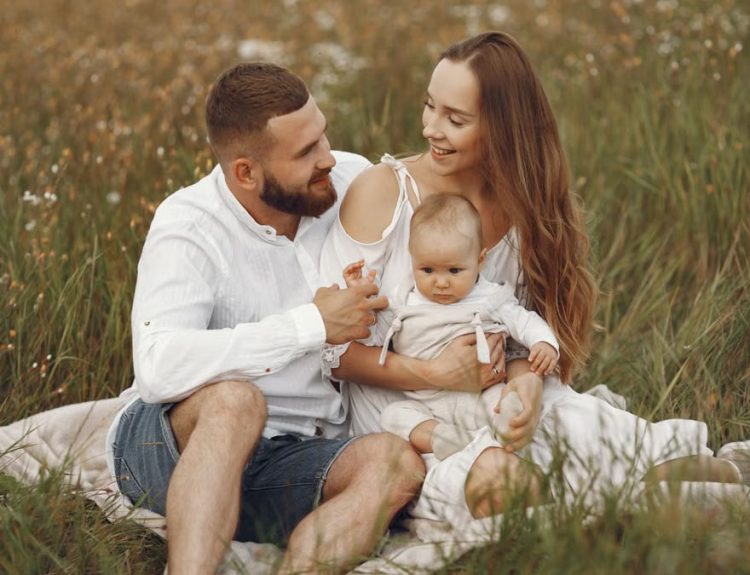 A joyful couple with their baby sitting on a blanket in a sunny meadow, embracing the beauty of summer.